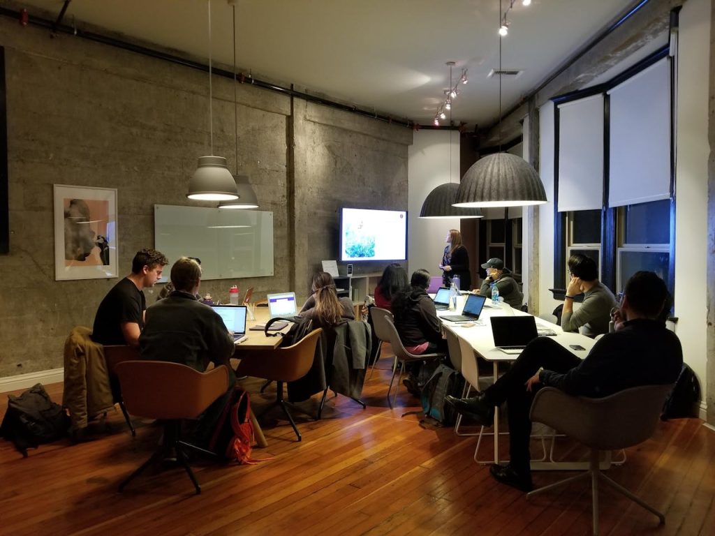 people-gathered-inside-one-room-2678468 Diverse team collaborating in a modern office setting with laptops and presentation screen.