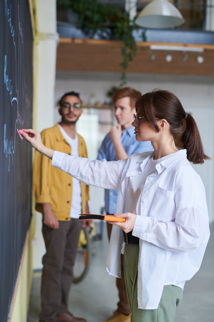 A group of young people discussing ideas at a blackboard in a modern office setting.